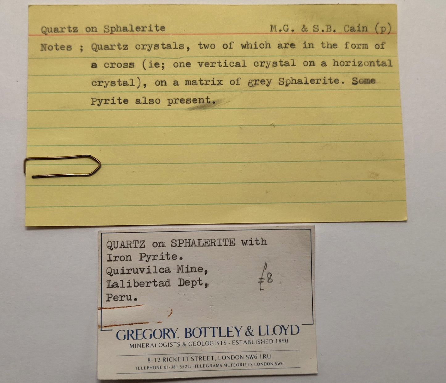 Yellowed paper card with handwritten text and a business card on a gray background