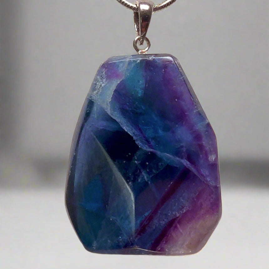 A polished fluorite pendant in shades of purple and blue, showing a unique benz formation, suspended from a silver plated chain.