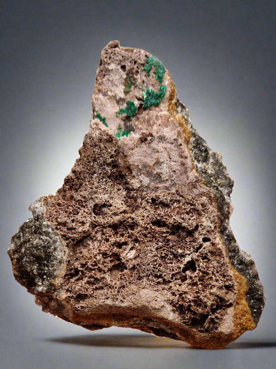 Rock with green mineral veins held by a hand against a neutral background