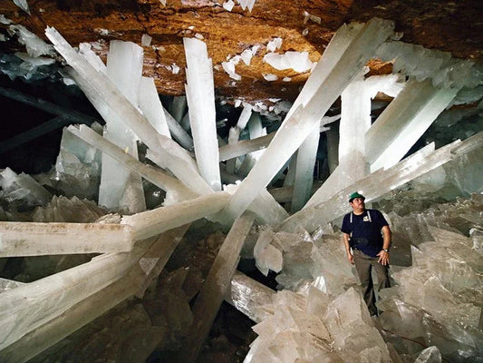 Man standing inside cave with giant clear crystal formations and minerals