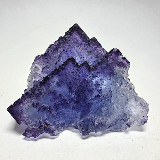 Close-up of a purple and blue crystal mineral specimen with layered geometric edges on white background