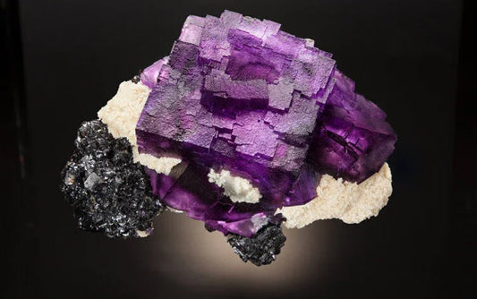 Purple cubic fluorite crystal cluster with white and black mineral matrix on dark background