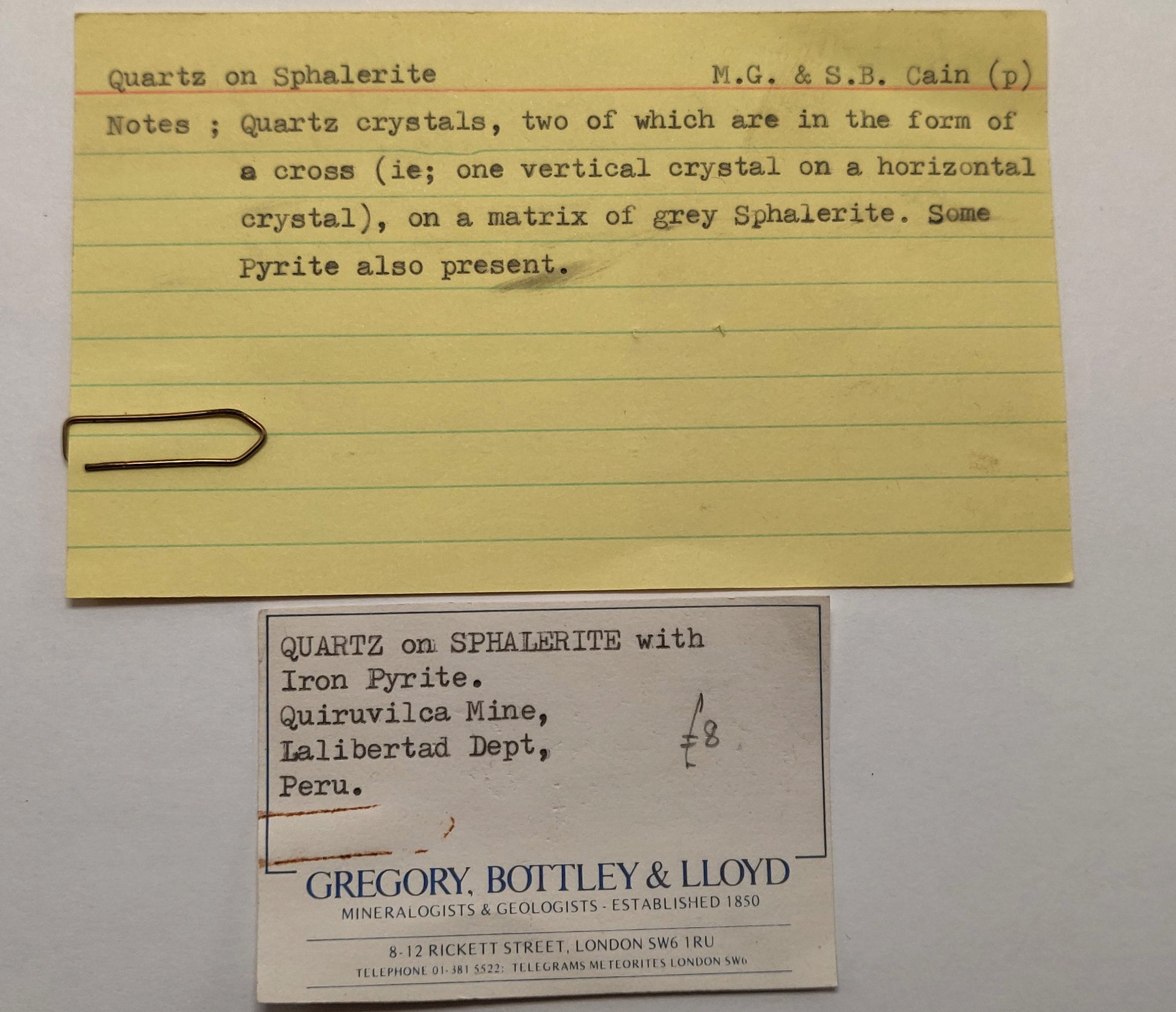 Yellowed paper card with handwritten text and a business card on a gray background