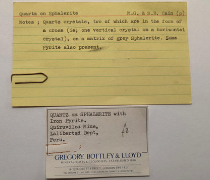 Yellowed paper card with handwritten text and a business card on a gray background