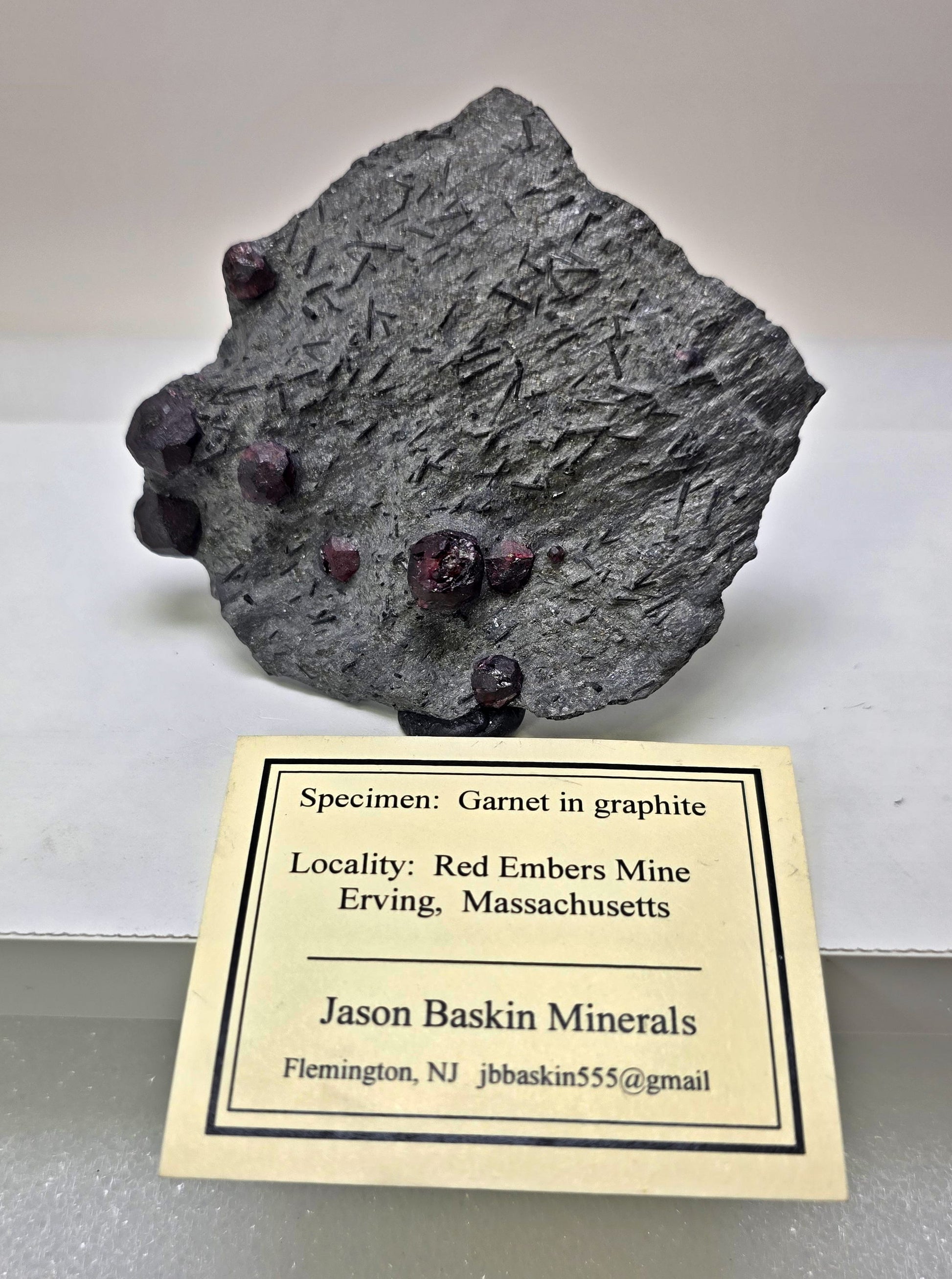 Mineral specimen with garnet in graphite on a label from Jason Baskin Minerals.