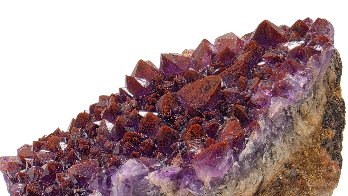 A natural amethyst crystal cluster with sharp purple and reddish-brown crystal points on a rough matrix, photographed against a plain light background.