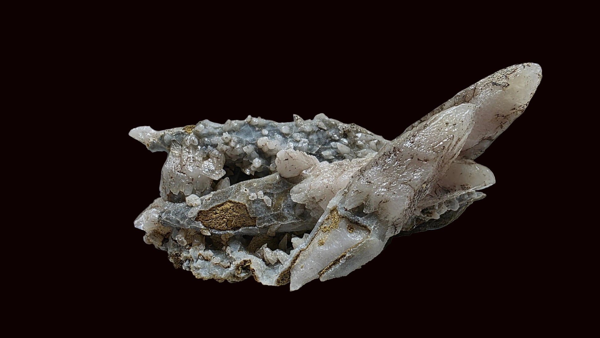 A natural mineral specimen featuring a cluster of pale pinkish-white quartz crystals and grayish-white calcite crystals with a small gold vein, displayed on a light gray surface.
