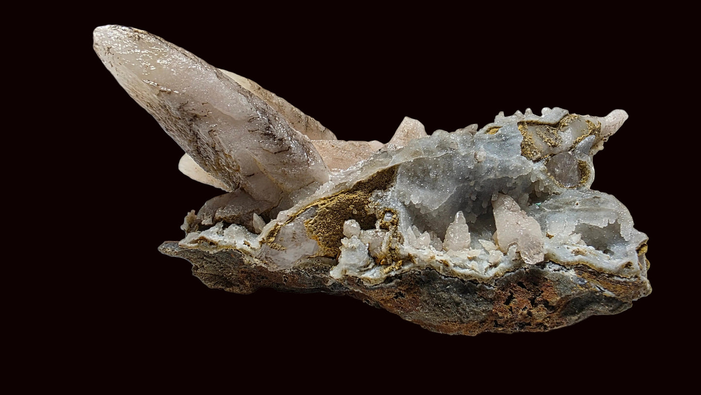 A natural mineral specimen featuring a large translucent pale crystal point rising from a rough, earthy matrix with gray and white crystalline areas, photographed on a plain light background.