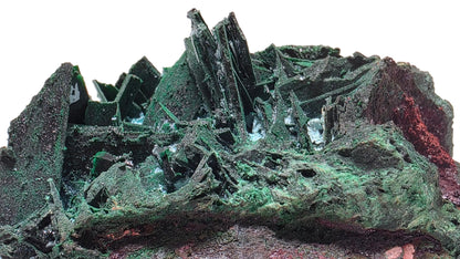 A close-up of a rough mineral or crystal cluster with prominent green crystalline structures and darker earthy brown and reddish areas, set against a soft pink background.