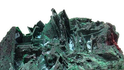 A close-up of a green mineral specimen with sharp crystalline structures and a dark textured matrix, photographed against a soft pink studio background.