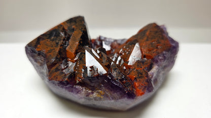A natural crystal cluster specimen with prominent orange-brown and purple crystalline structures, photographed on a plain light background.
