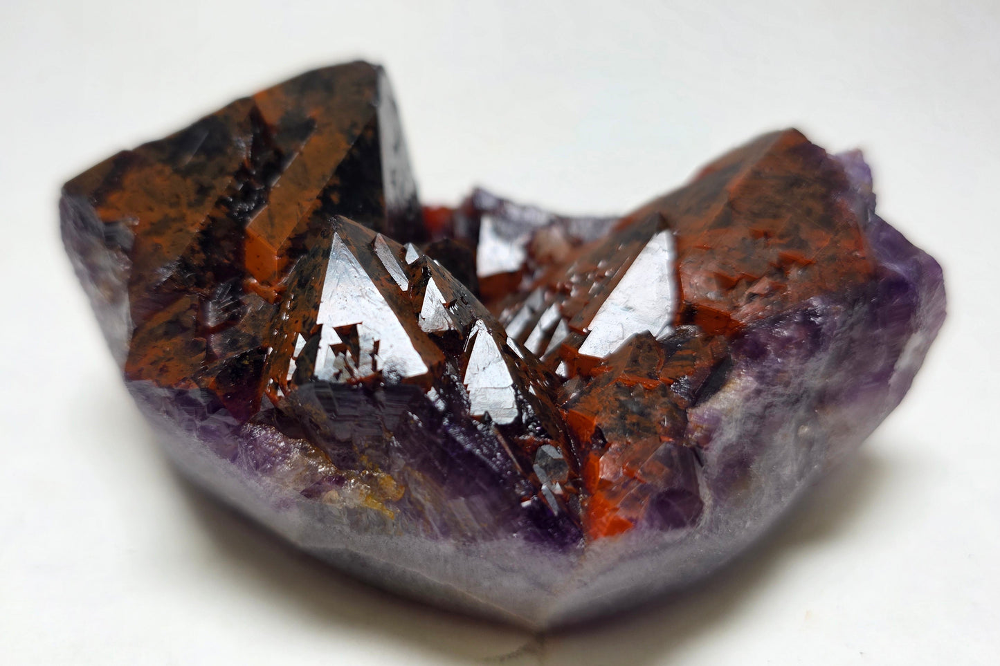 A raw amethyst crystal cluster with prominent dark brown and orange inclusions, set against a plain white background.