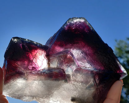 Person holding a large purple crystal against a blue sky with trees in the background