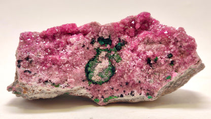 Pink crystal rock with green mineral inclusion on a white background
