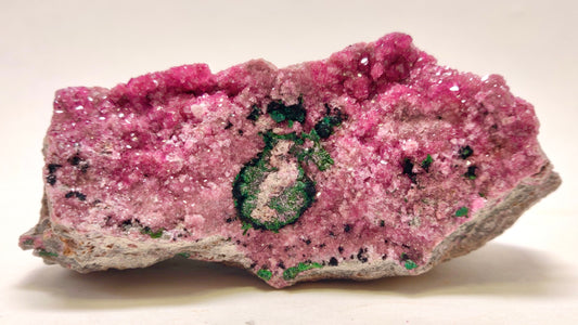 Pink crystal rock with green mineral inclusion on a white background