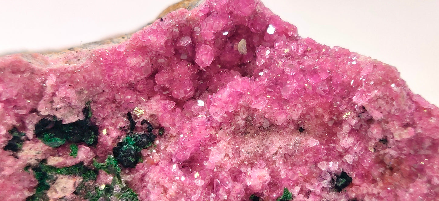 Close-up of a pink crystal formation with green minerals on a white background