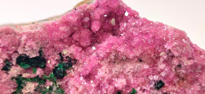 Close-up of a pink crystal formation with green minerals on a white background