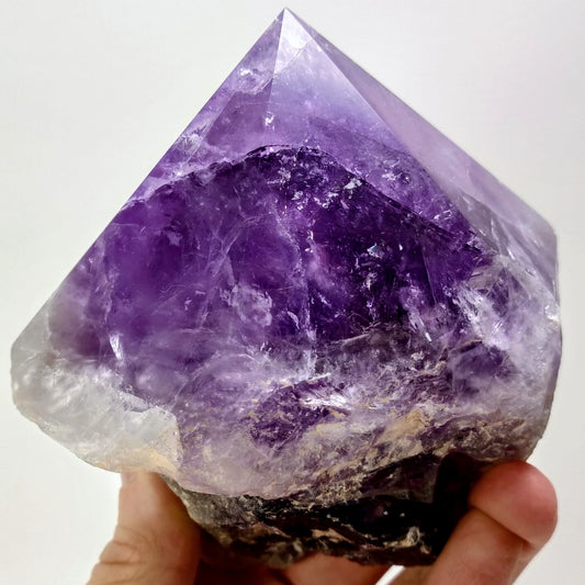 Amethyst crystal held in a hand against a white background