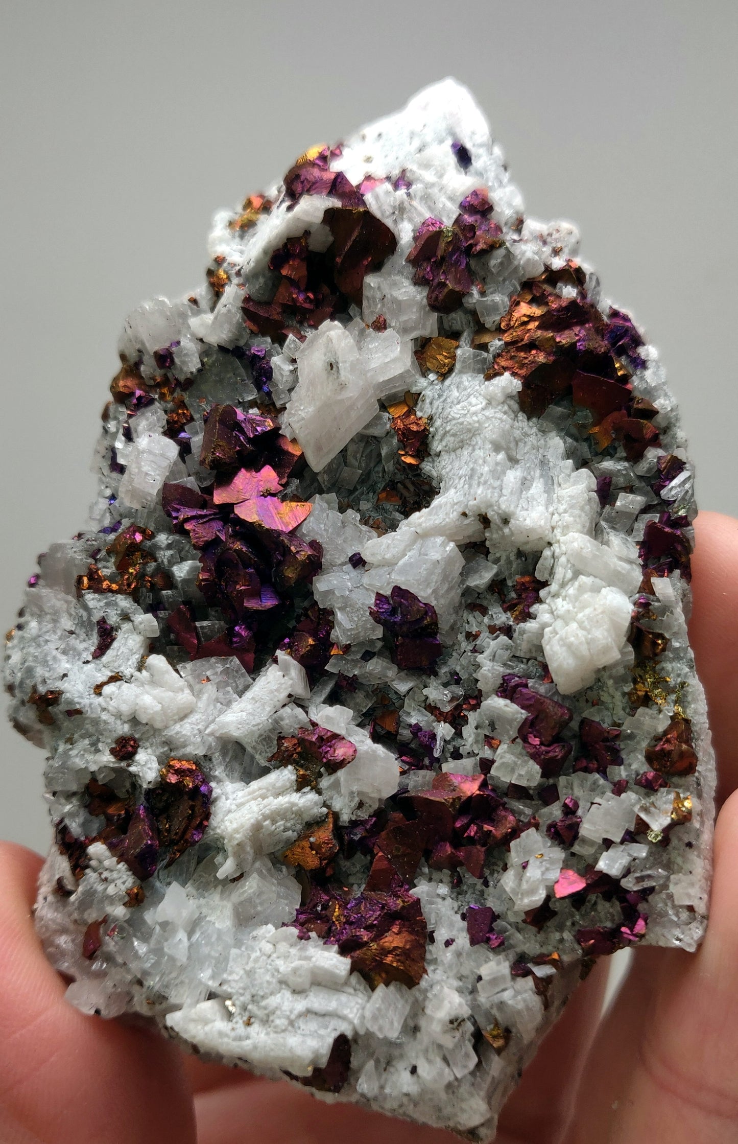 Iridescent rainbow chalcopyrite crystals on white rhombohedral calcite matrix from Baisha Mine, China.