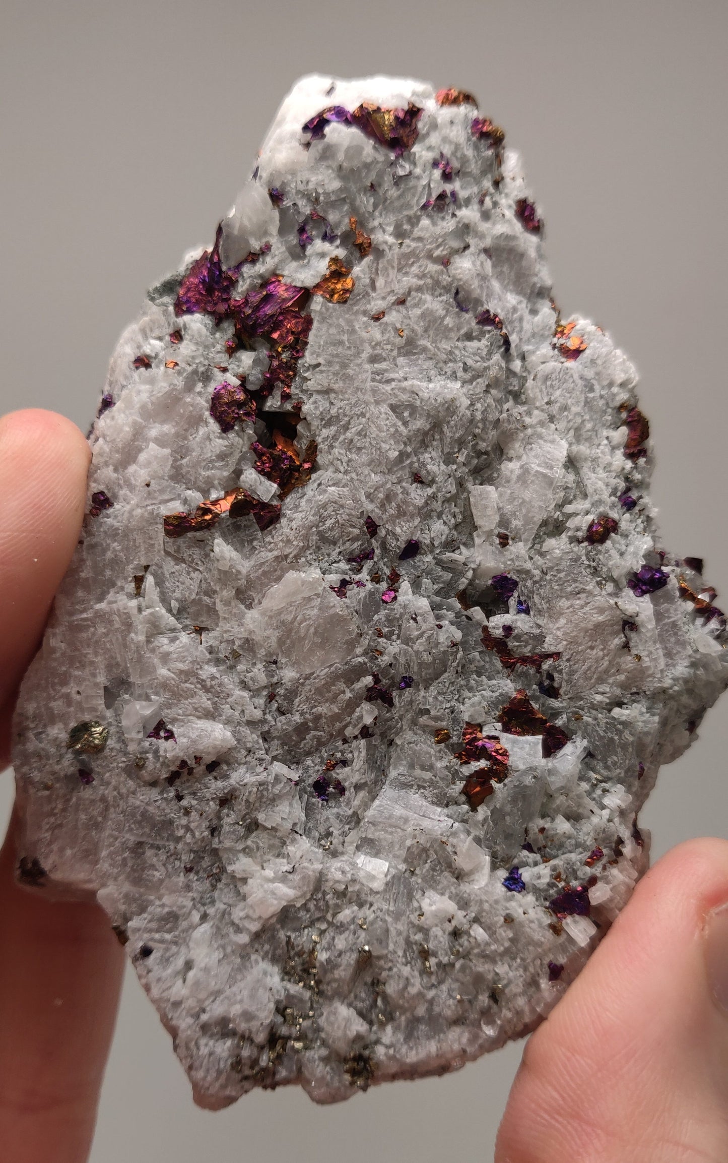 Iridescent rainbow chalcopyrite crystals on white rhombohedral calcite matrix from Baisha Mine, China.