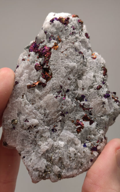 Iridescent rainbow chalcopyrite crystals on white rhombohedral calcite matrix from Baisha Mine, China.