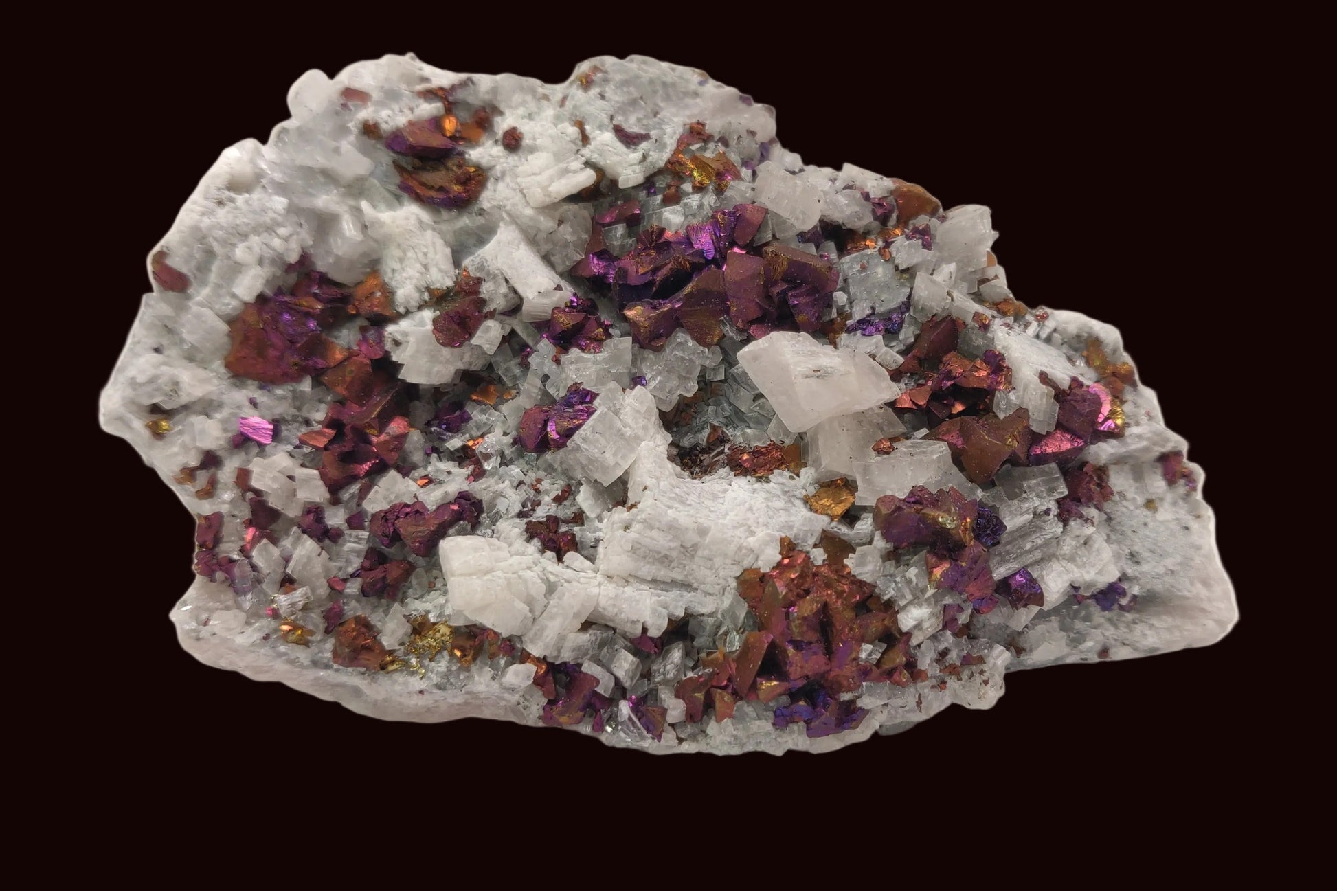 Iridescent rainbow chalcopyrite crystals on white rhombohedral calcite matrix from Baisha Mine, China.