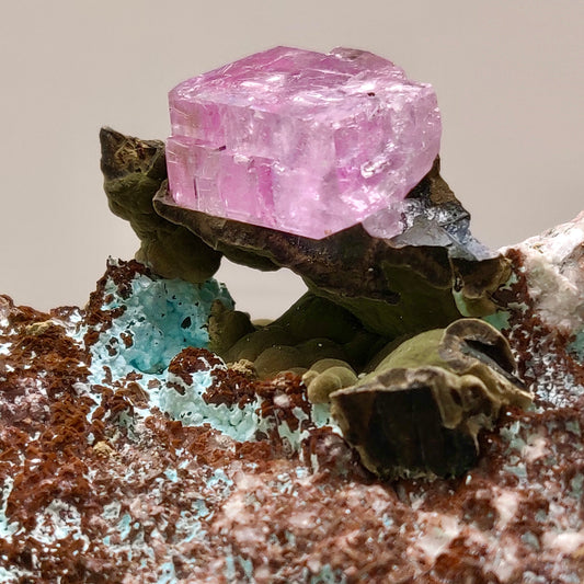 Pink crystal on a mineral rock with a neutral background