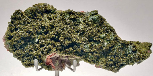A deep olive-green Epidote crystal cluster with a vitreous luster, set against its natural matrix, from Hakkçari Province, Turkey, displayed on a metal stand.