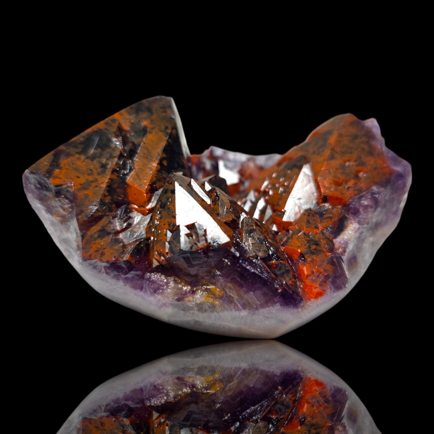 A polished crystal cluster specimen with prominent orange-brown and purple translucent sections, photographed on a black reflective surface.